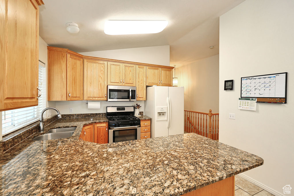 Kitchen featuring stainless steel appliances, a peninsula, lofted ceiling, dark stone counters, and light tile patterned floors