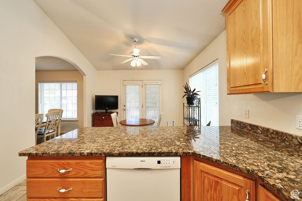 Kitchen featuring dishwasher, a peninsula, a ceiling fan, dark stone counters, and arched walkways