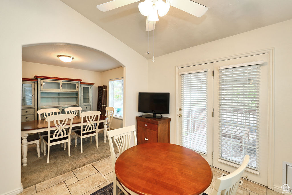 Dining room with arched walkways, vaulted ceiling, light tile patterned floors, a ceiling fan, and light carpet