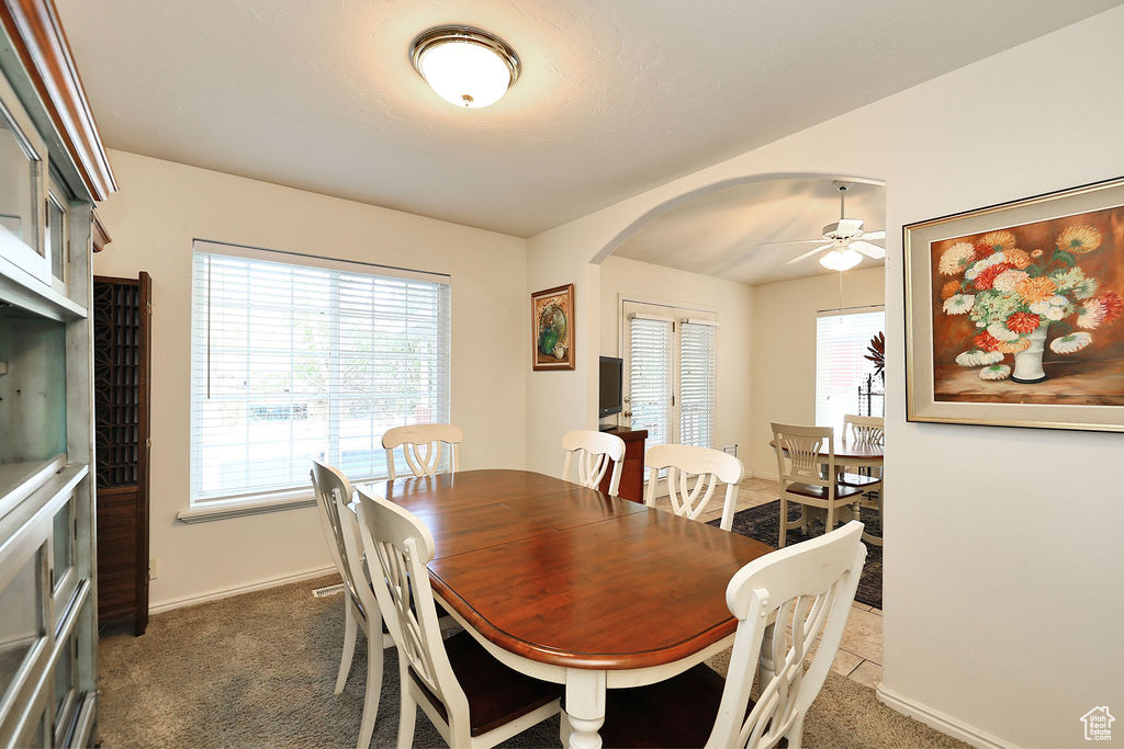Dining space with arched walkways, healthy amount of natural light, ceiling fan, and dark carpet