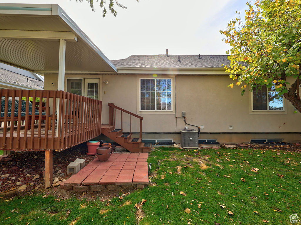 Rear view of property with a yard, stucco siding, a deck, and roof with shingles