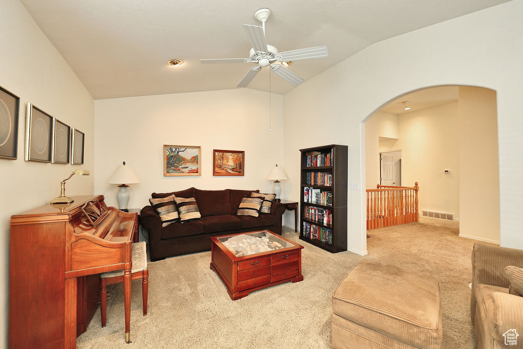 Carpeted living room with vaulted ceiling, ceiling fan, and arched walkways
