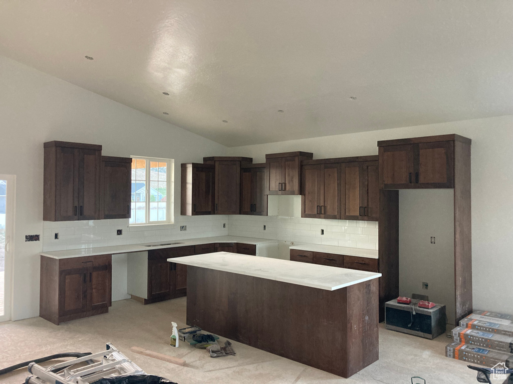 Kitchen featuring vaulted ceiling, decorative backsplash, a kitchen island, dark brown cabinetry, and light colored carpet
