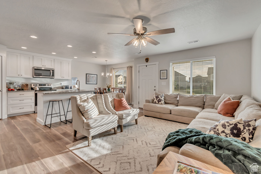 Living area featuring plenty of natural light, ceiling fan, light wood-type flooring, recessed lighting, and a chandelier