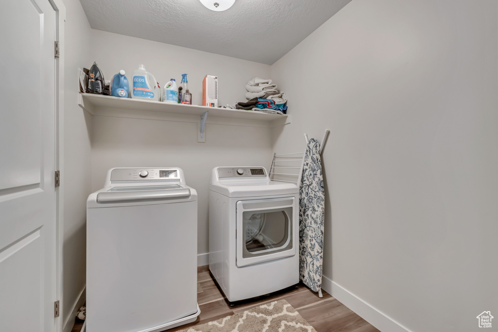 Laundry area featuring washing machine and dryer, light wood-style floors, and a textured ceiling