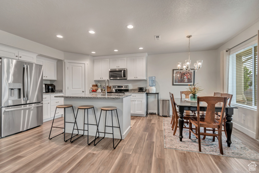 Kitchen with stainless steel appliances, light wood-style floors, a chandelier, white cabinetry, and recessed lighting