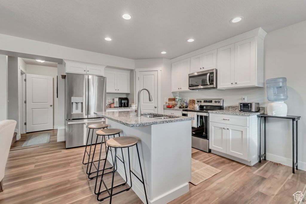 Kitchen with appliances with stainless steel finishes, light wood-type flooring, white cabinetry, light stone counters, and recessed lighting