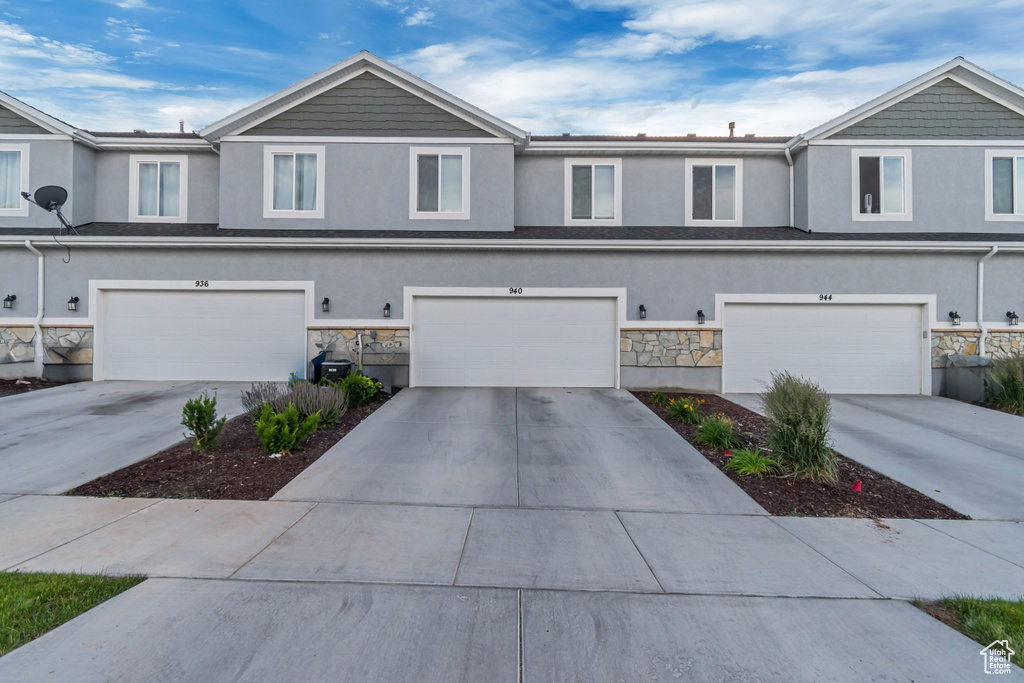 View of front facade featuring stucco siding, stone siding, an attached garage, and driveway