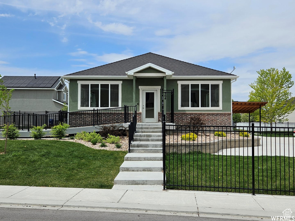 Bungalow-style home with stucco siding, a fenced front yard, brick siding, and a shingled roof