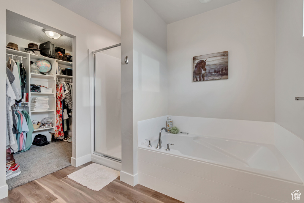 Bathroom featuring a spacious closet, a bath, a stall shower, and wood finished floors