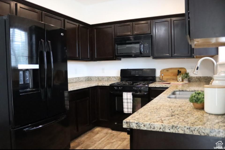 Kitchen featuring black appliances, dark brown cabinets, light wood-type flooring, and light stone counters