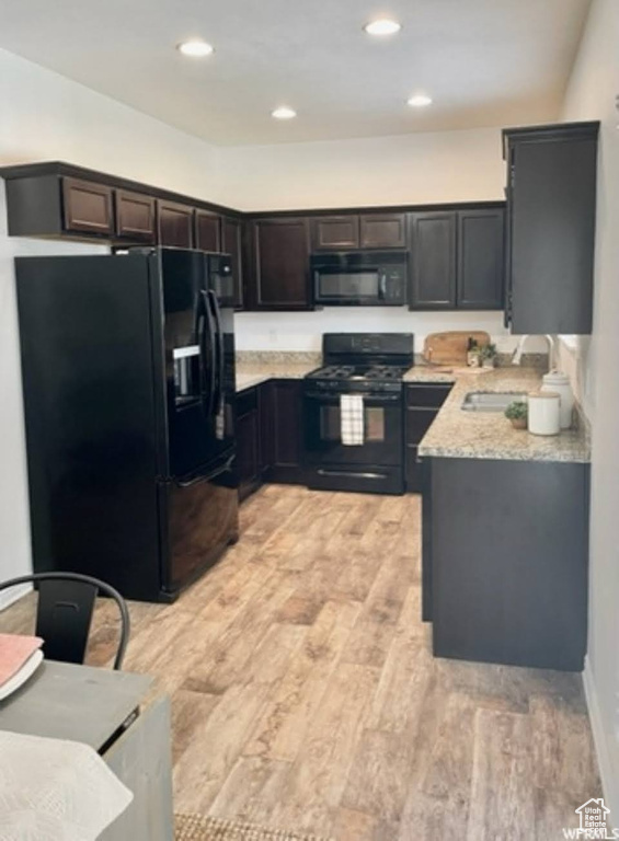 Kitchen featuring black appliances, light wood-style floors, light stone counters, and recessed lighting