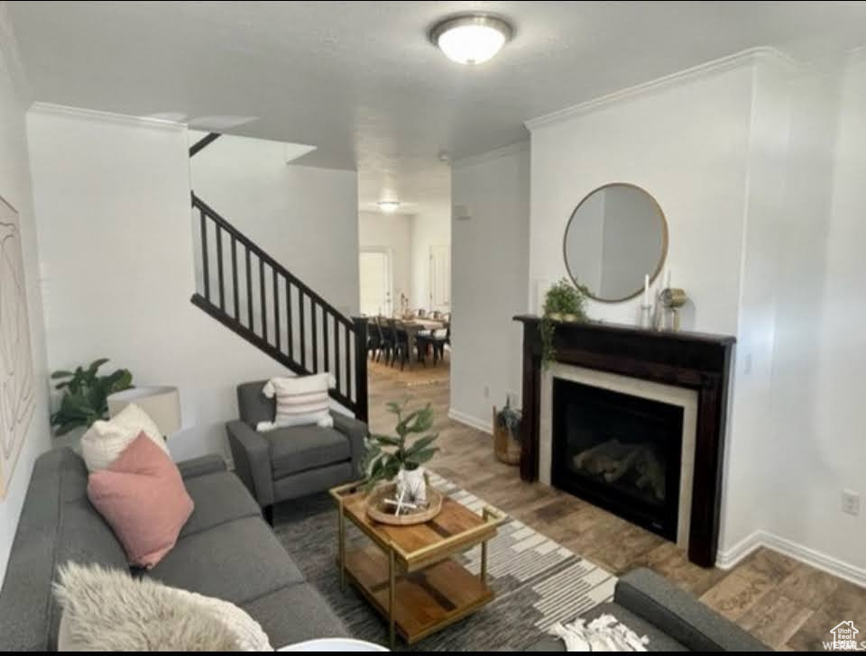Living area featuring stairway, crown molding, wood finished floors, and a fireplace