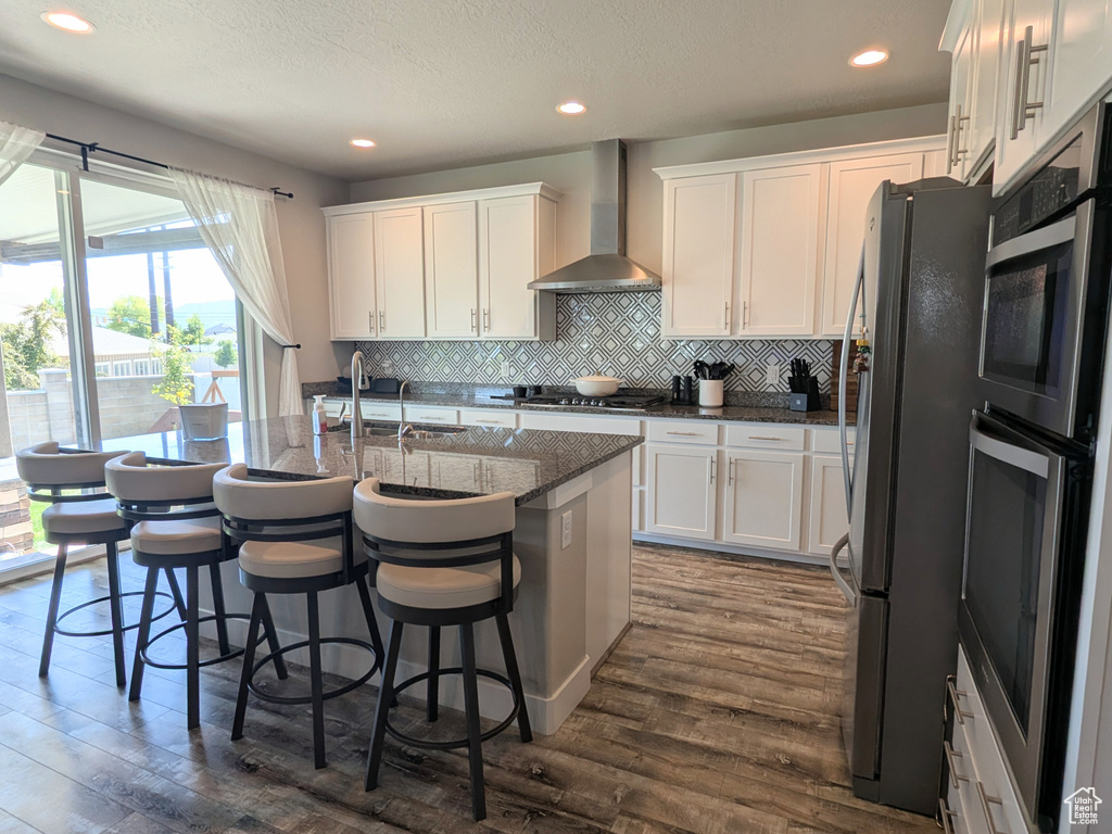 Kitchen featuring wall chimney range hood, freestanding refrigerator, white cabinets, and recessed lighting
