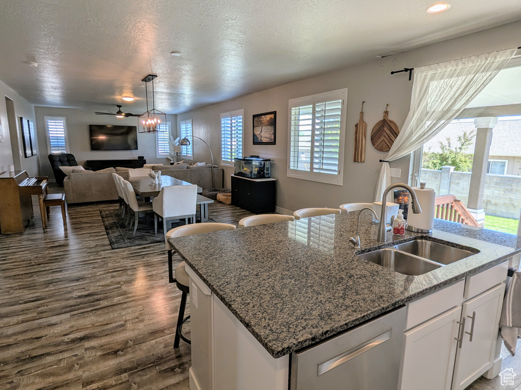 Kitchen featuring dishwasher, open floor plan, a center island with sink, dark wood-style flooring, and a ceiling fan