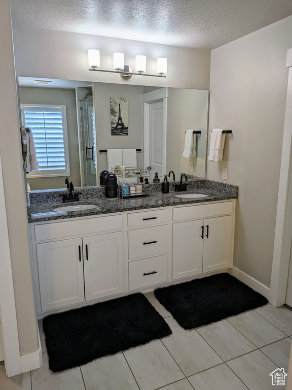 Full bath with double vanity, a textured ceiling, a stall shower, and tile patterned floors