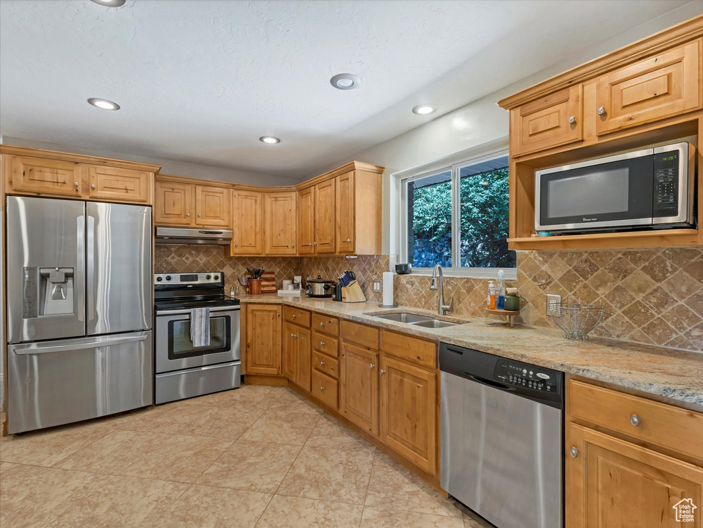 Kitchen featuring appliances with stainless steel finishes, under cabinet range hood, light stone countertops, tasteful backsplash, and recessed lighting