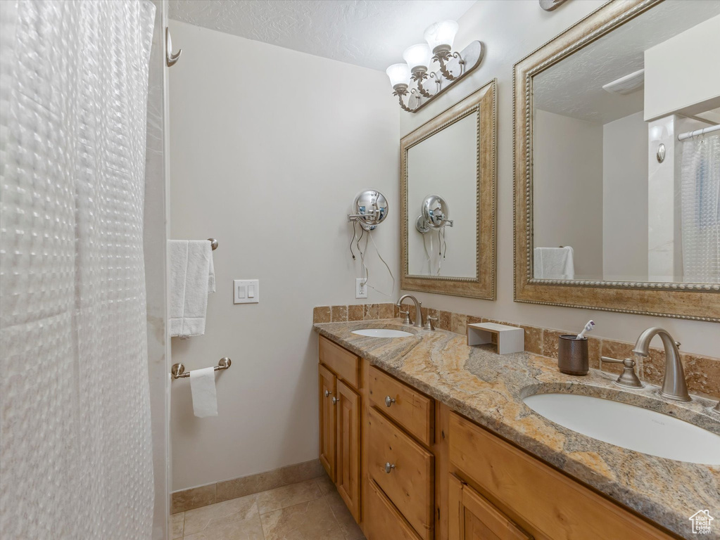 Bathroom with double vanity, tile patterned floors, and a shower with curtain