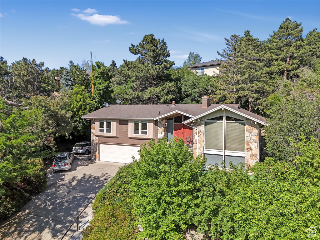 View of front of property featuring stone siding, driveway, an attached garage, and a chimney