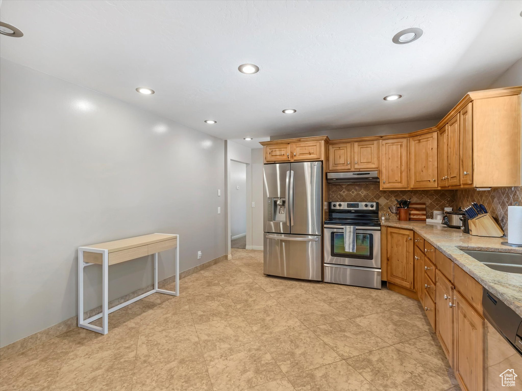 Kitchen with stainless steel appliances, under cabinet range hood, decorative backsplash, recessed lighting, and light stone counters