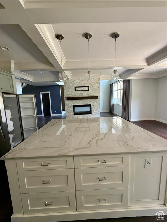 Kitchen featuring a kitchen island, light stone countertops, white cabinetry, hanging light fixtures, and beamed ceiling