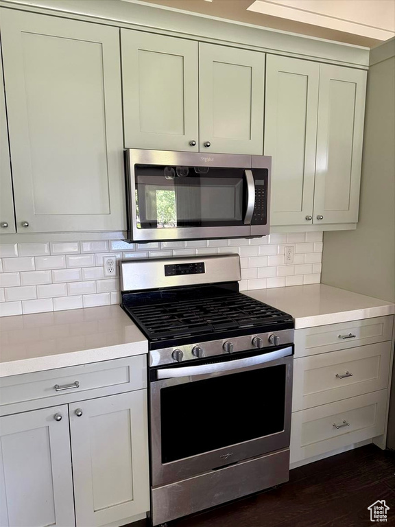 Kitchen featuring appliances with stainless steel finishes, light countertops, backsplash, and dark wood-type flooring