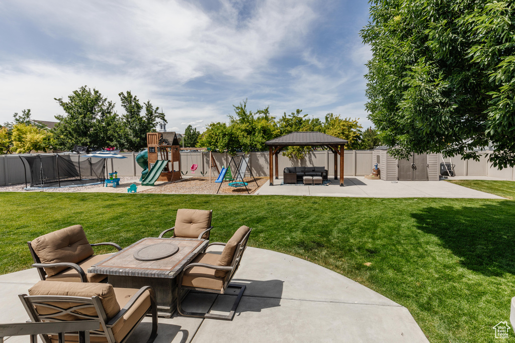 Fenced backyard with a patio area, an outdoor hangout area, a shed, a playground, and a trampoline