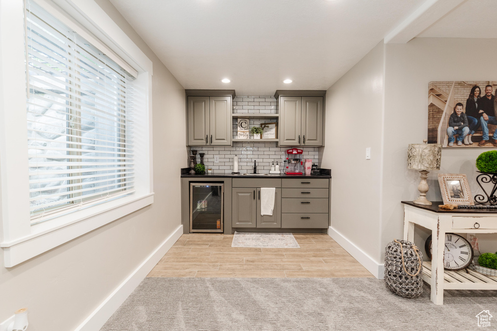 Indoor wet bar with beverage cooler, backsplash, recessed lighting, and light wood finished floors