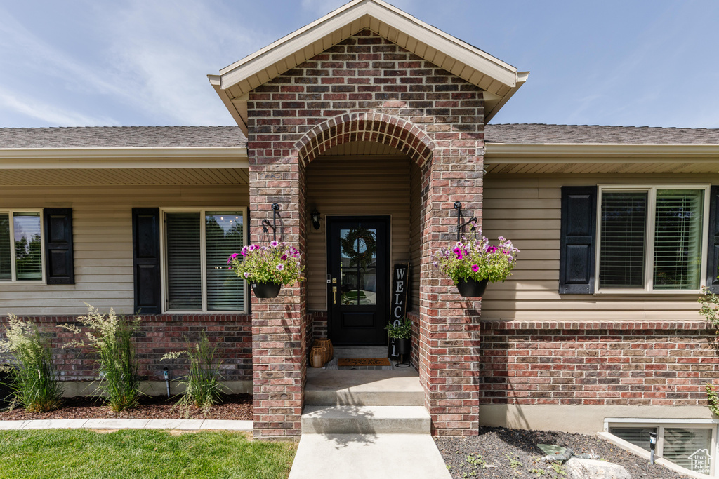 View of exterior entry featuring brick siding and a shingled roof