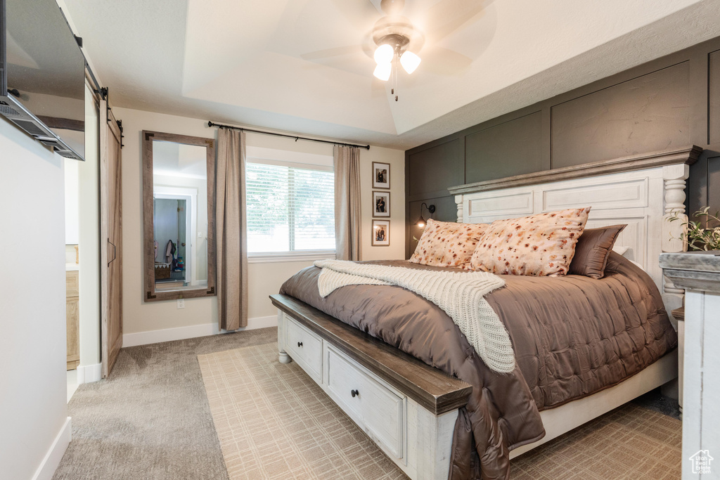 Bedroom featuring a raised ceiling, light carpet, a barn door, and ceiling fan