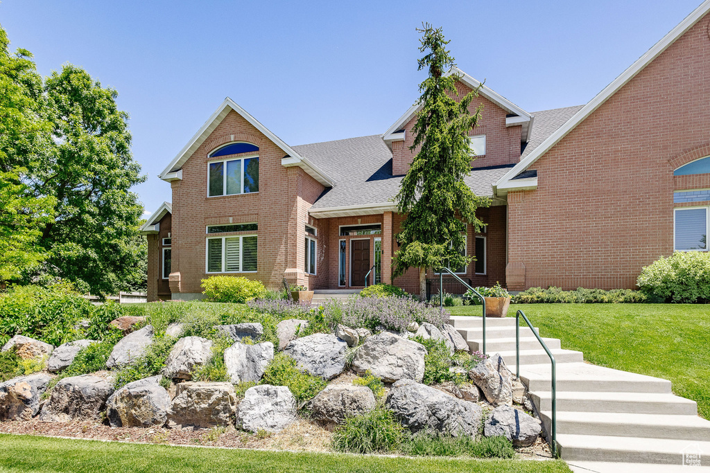 View of front of house with brick siding, a shingled roof, and a front yard