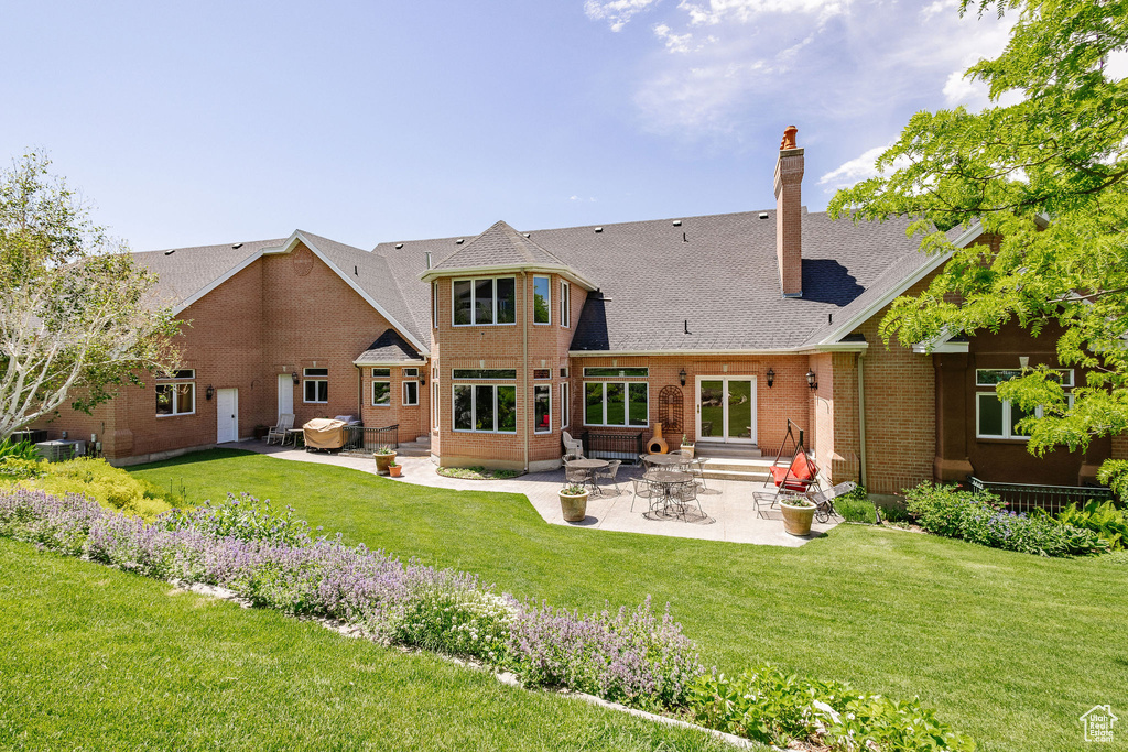 Rear view of property featuring a patio, entry steps, a yard, a chimney, and brick siding