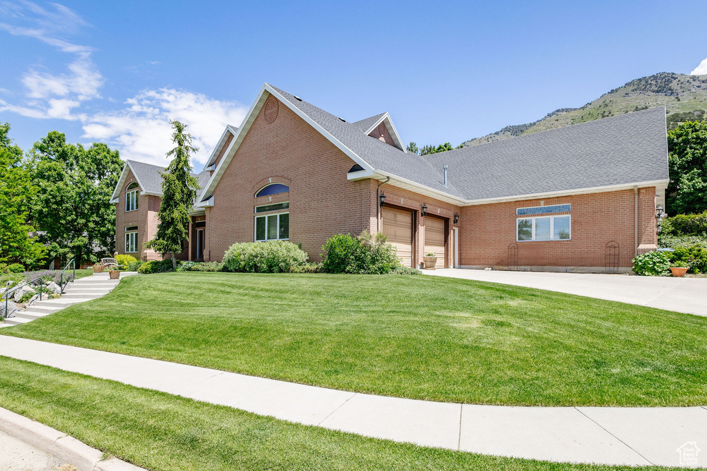 View of front facade featuring brick siding, an attached garage, a front yard, concrete driveway, and a mountain view