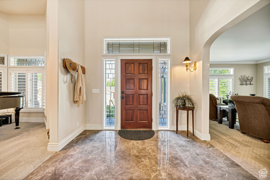 Foyer entrance with arched walkways, a high ceiling, carpet floors, marble finish flooring, and crown molding
