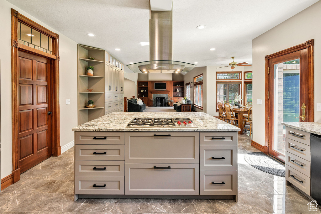 Kitchen featuring stainless steel gas stovetop, ceiling fan, island range hood, marble tiled floors, and gray cabinetry