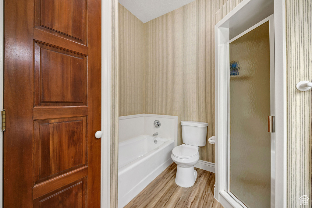 Bathroom with wallpapered walls, wood finished floors, a bath, and a shower stall