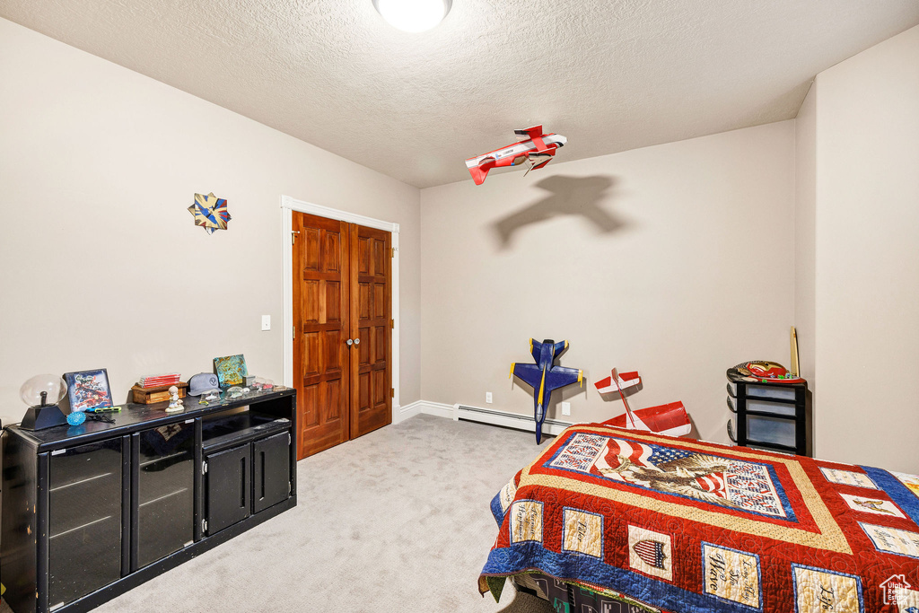 Carpeted bedroom featuring baseboard heating and a textured ceiling