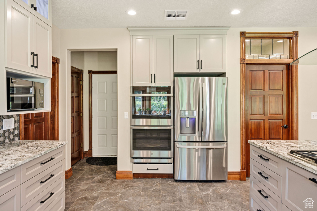 Kitchen with stainless steel appliances, marble finish flooring, light stone countertops, white cabinets, and recessed lighting