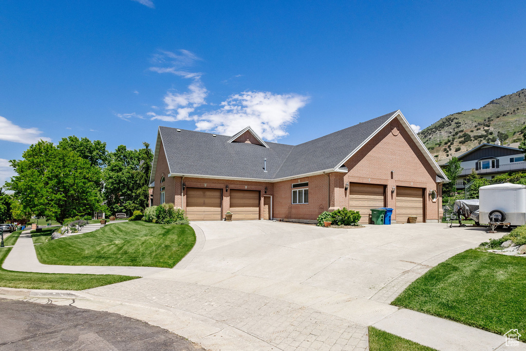 View of front of property featuring brick siding, a front lawn, an attached garage, a mountain view, and driveway