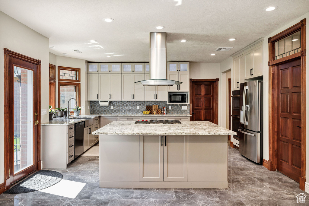 Kitchen featuring freestanding refrigerator, island exhaust hood, dishwashing machine, black microwave, and gas cooktop