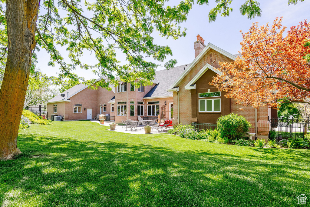 Rear view of house featuring brick siding, a lawn, a patio area, and a chimney