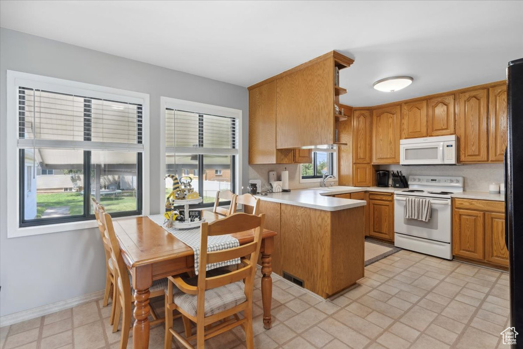 Kitchen with white appliances, a peninsula, light countertops, and brown cabinets