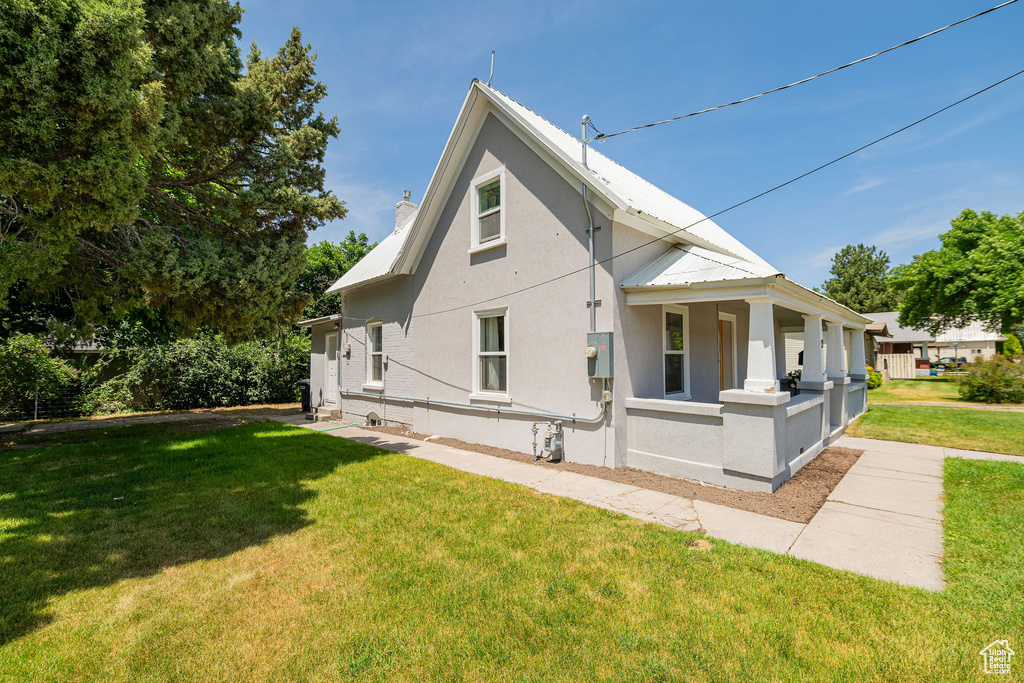 Back of house with stucco siding, a yard, a porch, and a metal roof