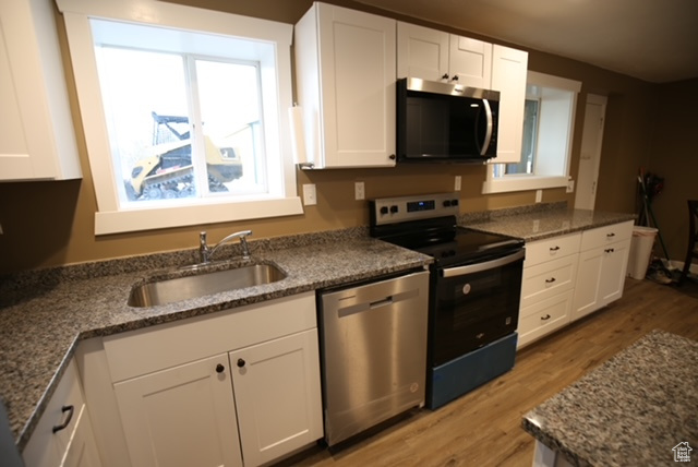 Kitchen featuring stainless steel appliances, light wood-type flooring, white cabinets, and dark stone counters