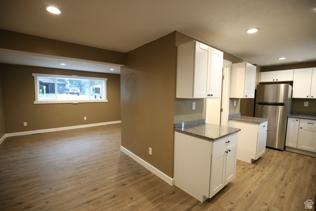 Kitchen featuring freestanding refrigerator, white cabinetry, light wood-style flooring, dark stone countertops, and recessed lighting