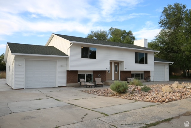 Raised ranch featuring an attached garage, concrete driveway, and a chimney