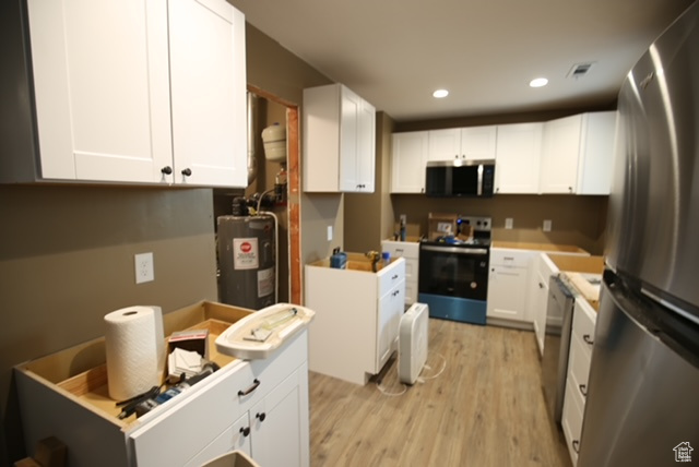 Kitchen featuring stainless steel appliances, water heater, light wood-type flooring, white cabinets, and recessed lighting