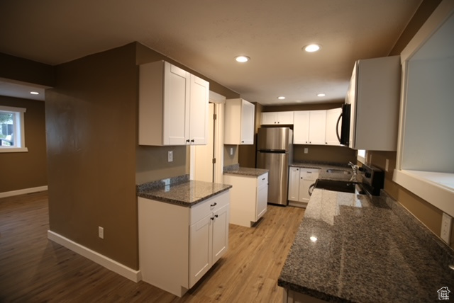 Kitchen featuring freestanding refrigerator, stove, black microwave, light wood-style flooring, and recessed lighting