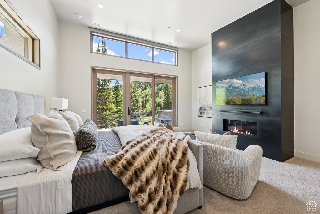 Bedroom featuring access to outside, a large fireplace, a towering ceiling, carpet floors, and recessed lighting