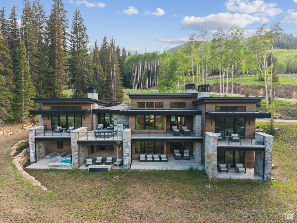 Back of property with a patio area, stone siding, a view of trees, and a balcony